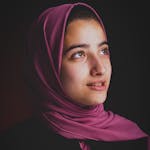 A beautiful portrait of a young woman wearing a pink hijab, captured in a studio setting.