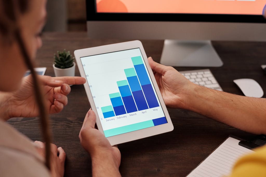 Two adults working in an office, examining graphs on a tablet screen for data analysis.