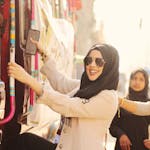 Woman in hijab and sunglasses climbing a decorated bus on a sunny day.